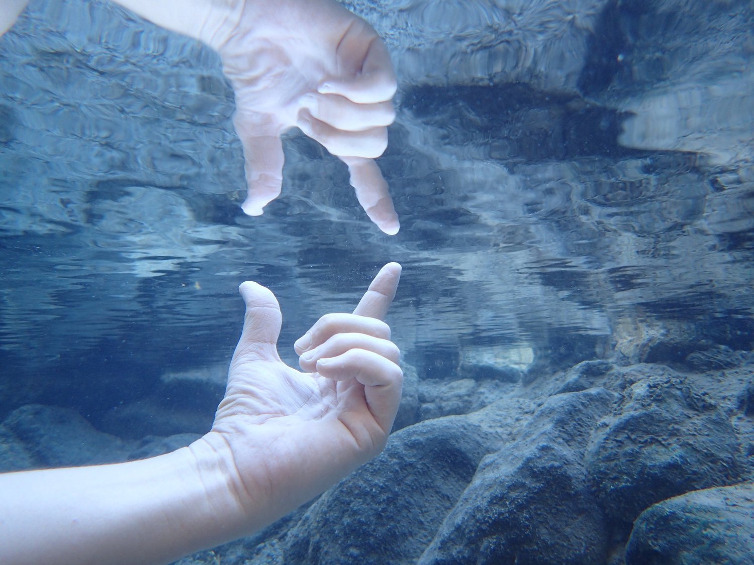 Two hands reaching toward each other beneath clear river water